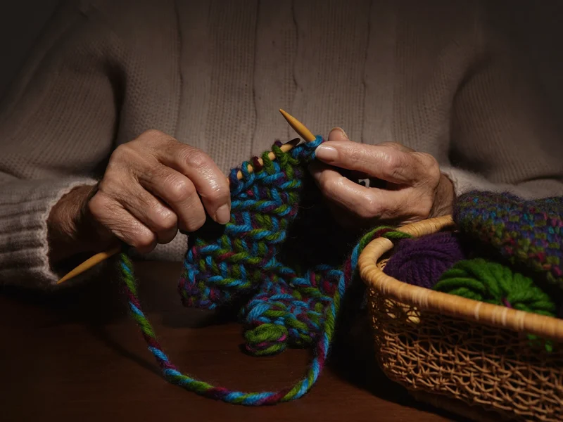 Mani di donna anziana che lavorano a maglia con lana colorata